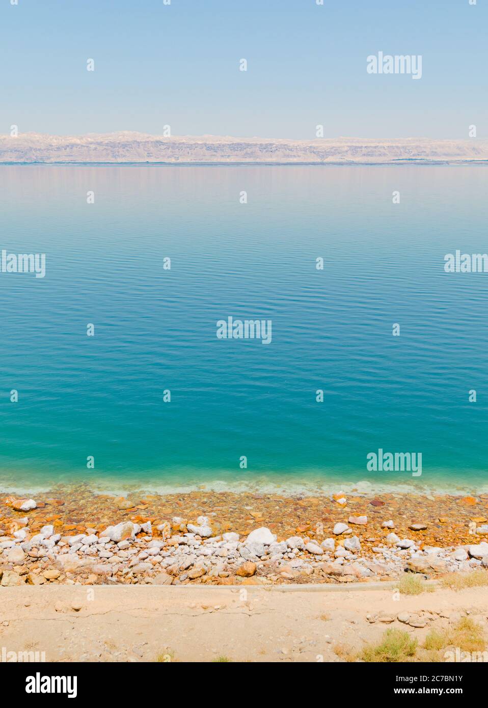 Vue verticale sur le littoral de la mer Morte, avec une croûte de sel et une plage de galets près d'une station touristique, et la ligne de montagne des territoires d'Israël sur le hor Banque D'Images