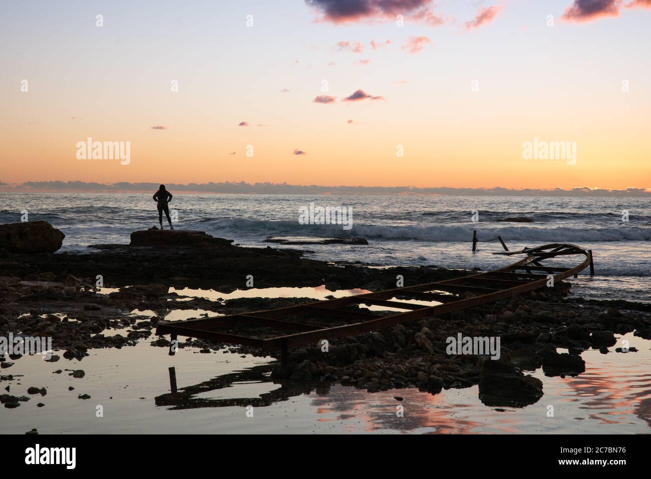 Silhouette de femme qui regarde loin de la mer Méditerranée, près d'un quai en métal abandonné sur une plage, au coucher du soleil, à Batroun, Liban, Middel est Banque D'Images