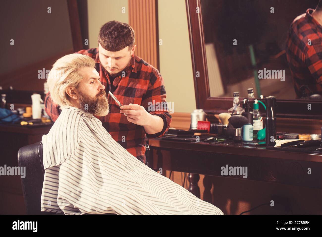 Homme blond brutal ayant une coupe de cheveux au salon de coiffure. Coiffeur mains faisant la coiffure. Banque D'Images