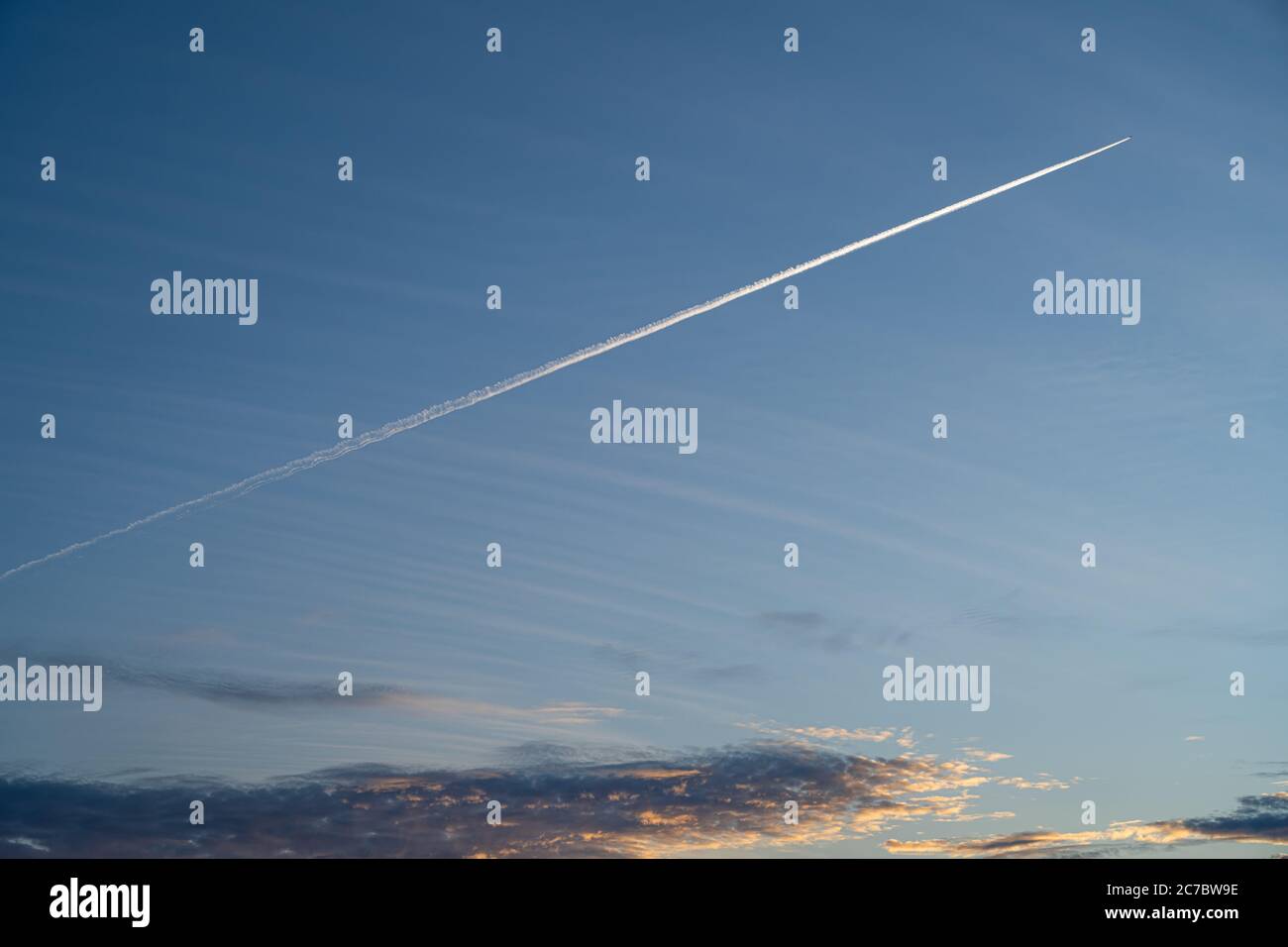 Un avion laisse une ligne de vapeur blanche sur un magnifique ciel bleu de coucher de soleil. Ciel bleu, nuages sombres et coucher de soleil orange Banque D'Images