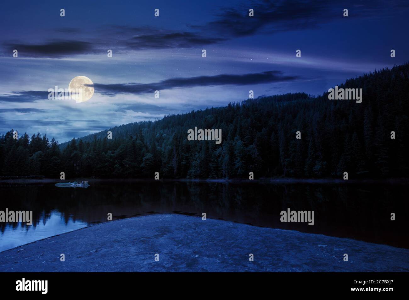 paysage autour du lac en montagne la nuit. forêt d'épicéa sur la rive. réflexion dans l'eau en pleine lumière de lune. temps avec nuages sur le ciel Banque D'Images