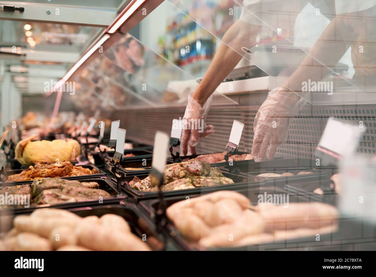 Gros plan des morceaux de viande crue dans le réfrigérateur avec des étiquettes de prix prêtes à être vendues dans le rayon de la viande du magasin. Les hommes mettent en place une assiette en verre avec des steaks frais en tranches. Concept de nourriture. Banque D'Images