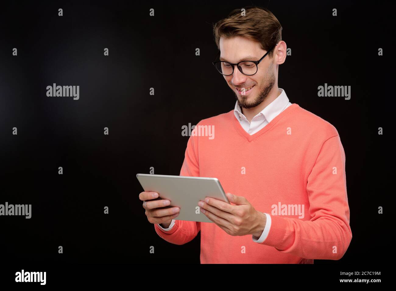 Souriant beau jeune barbu dans un chandail brillant surfant sur les médias sociaux sur tablette numérique sur un fond isolé Banque D'Images