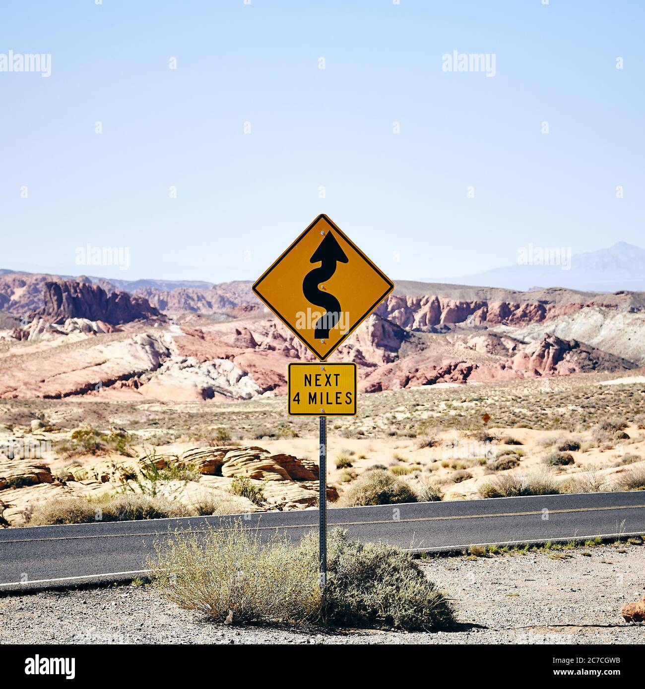 Panneau de route courbe jaune sur la route entourée de montagnes rocheuses dans la Vallée de feu, Nevada Banque D'Images