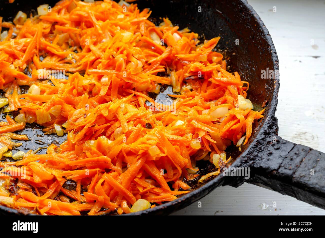 Morceaux d'oignons frits et de carottes dans une poêle. Les oignons coupés en dés et les carottes râpées sont frits sur le poêle. Cuisine. Plats faits maison. Mise au point sélective Banque D'Images