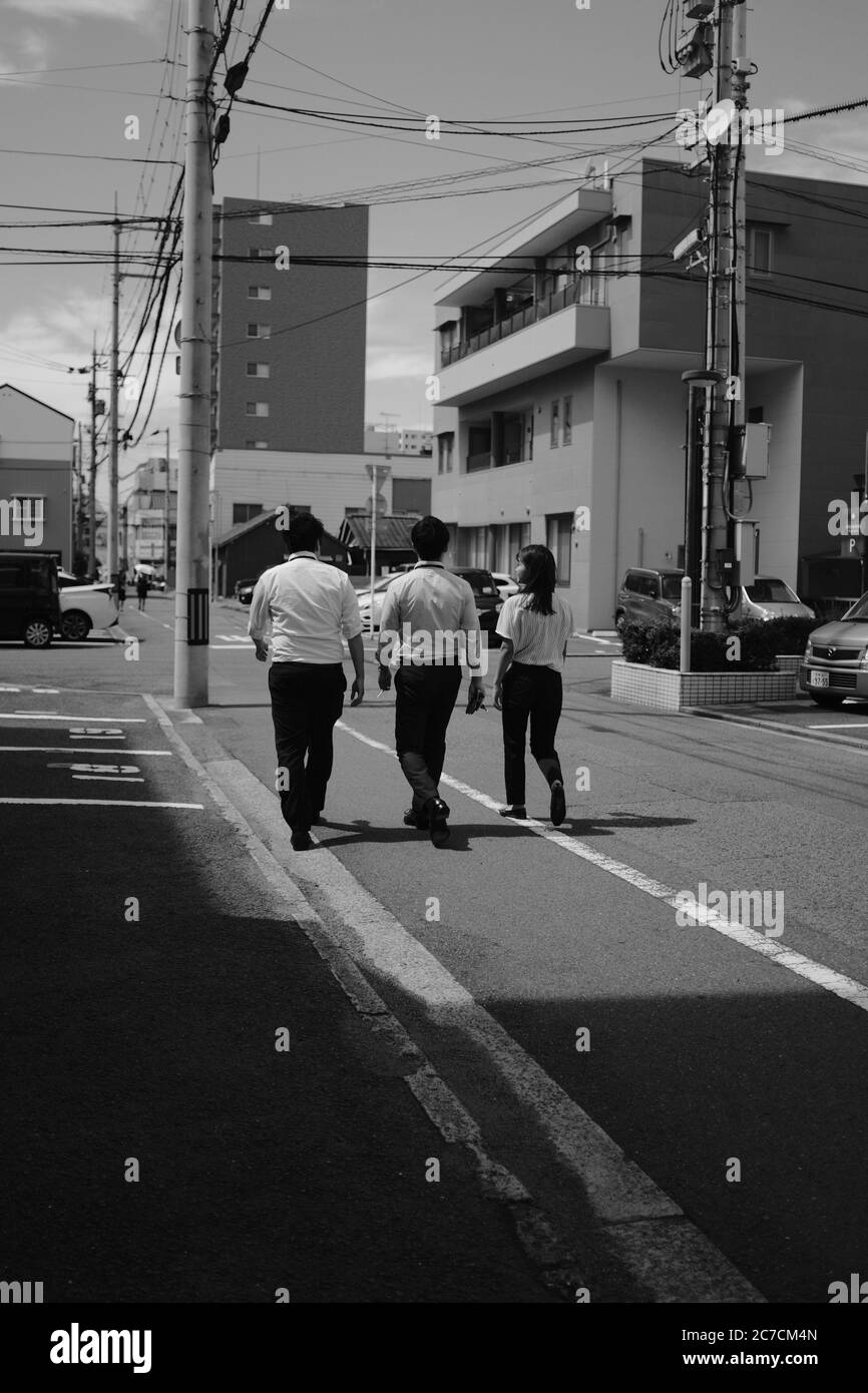 MATSUYAMA, JAPON - 14 septembre 2019 : une photo verticale en niveaux de gris de trois amis marchant dans la rue pendant la journée Banque D'Images