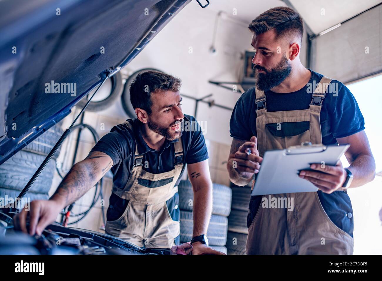 Jeunes mécaniciens automobiles qui changent l'huile lors de la réparation du moteur d'une voiture dans un atelier. Banque D'Images