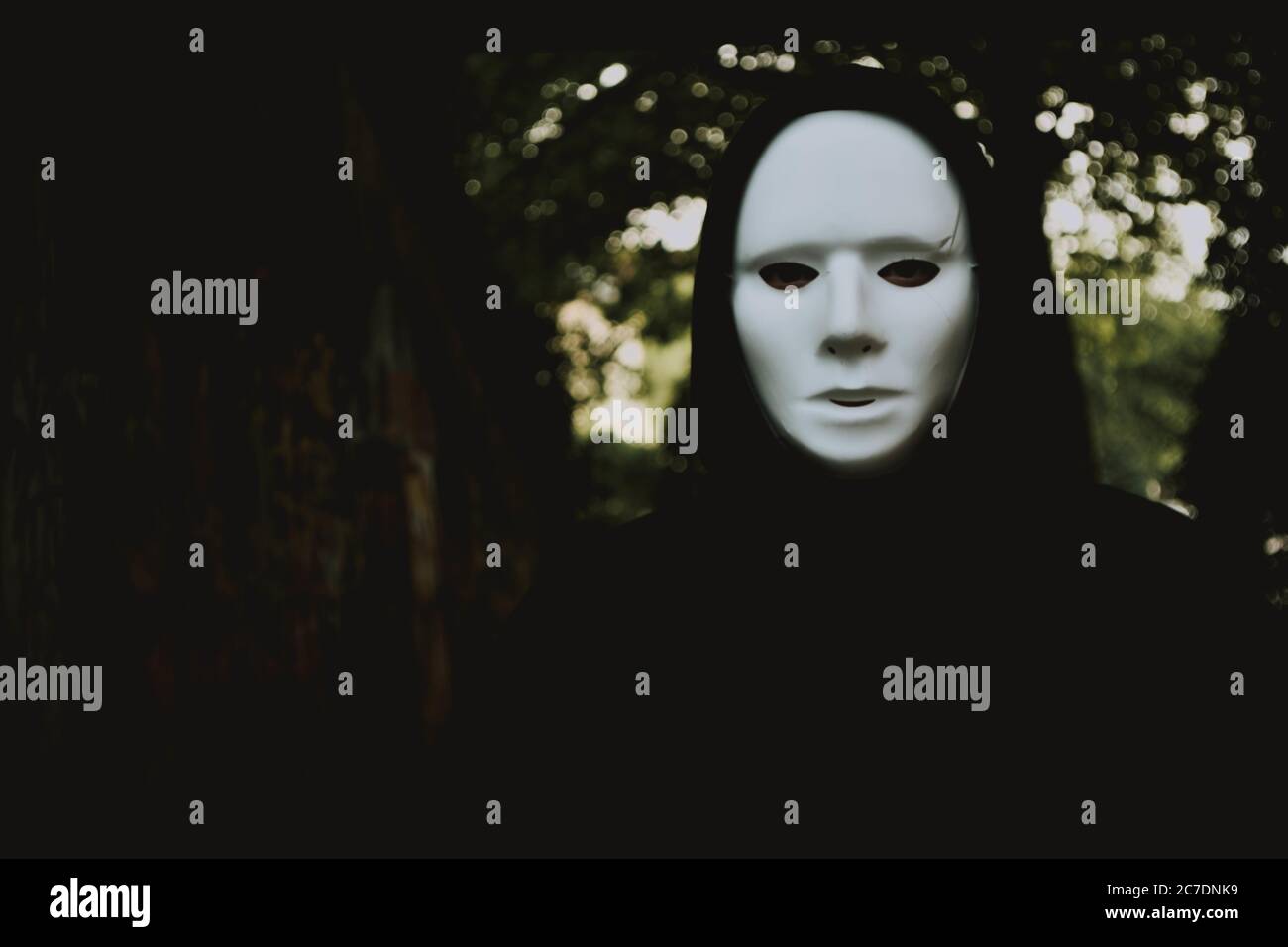 Gros plan sélectif d'une personne à capuchon noire portant du blanc masque sur le fond flou des arbres Banque D'Images