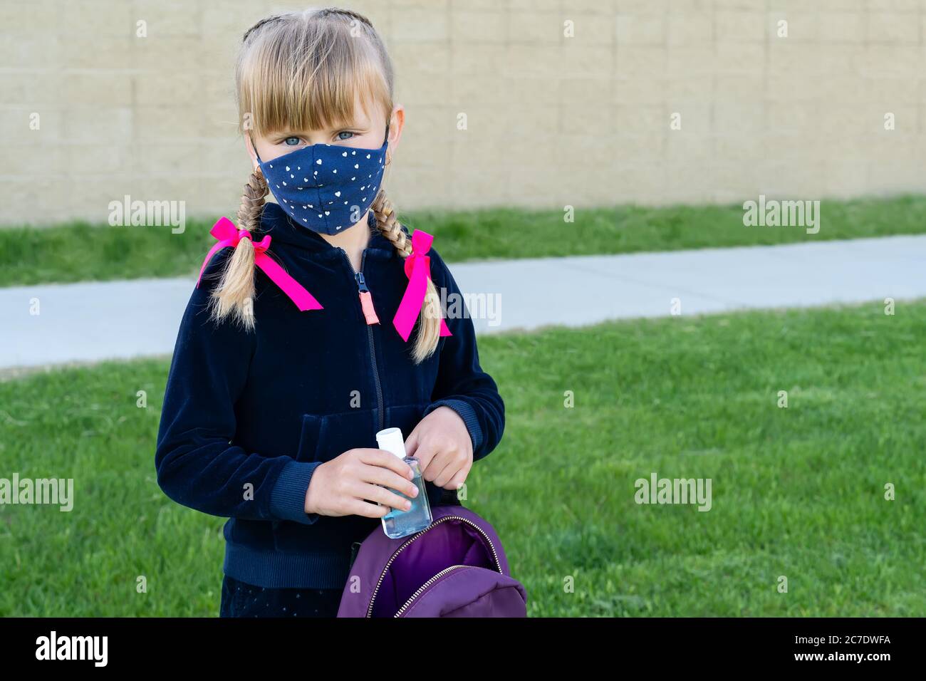 Jeune fille caucasienne portant un masque de protection en coton pour l'école et portant un désinfectant pour les mains. Retour à l'école, réouverture, Banque D'Images