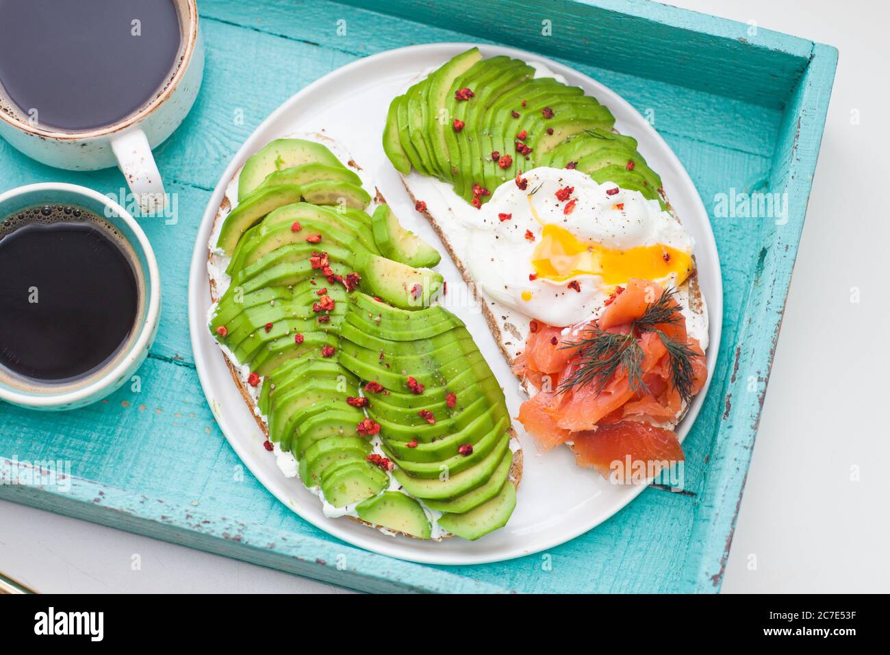 Bruschetta au saumon salé, avocat haché, poivre et œuf poché sur une assiette blanche sur fond de turqoise Banque D'Images