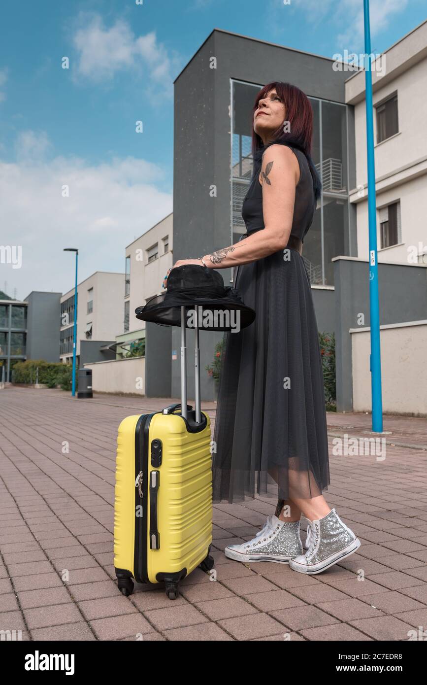 Femme touristique en robe vintage tenant une valise sur une place de la ville. Banque D'Images