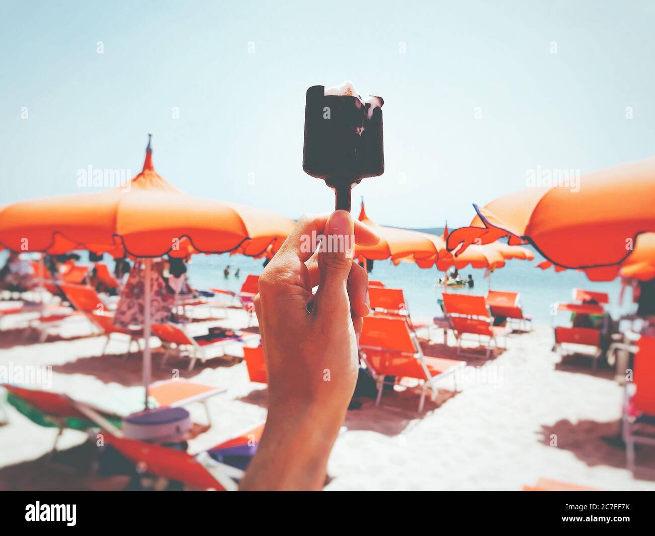 Une personne tenant une glace au chocolat bitten avec des chaises orange et parasols en arrière-plan Banque D'Images