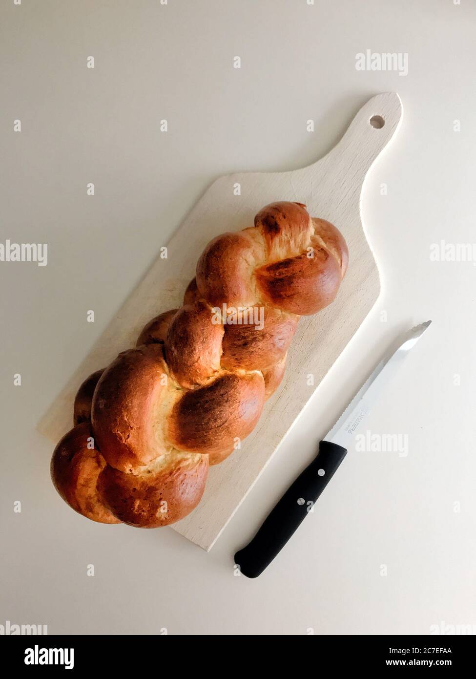 Plan vertical à angle élevé de challah sur un hacher blanc planche à côté d'un couteau sur une surface blanche Banque D'Images