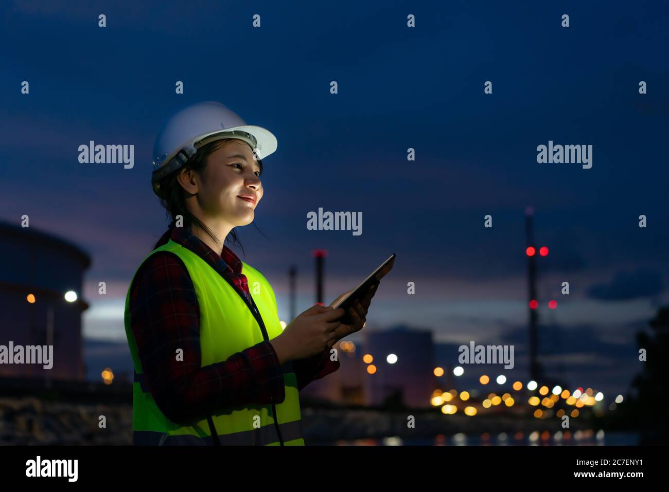 Femme asiatique ingénieur pétrochimique travaillant la nuit avec une tablette numérique à l'intérieur de l'usine de raffinage de pétrole et de gaz la nuit pour la sécurité des inspecteurs Banque D'Images