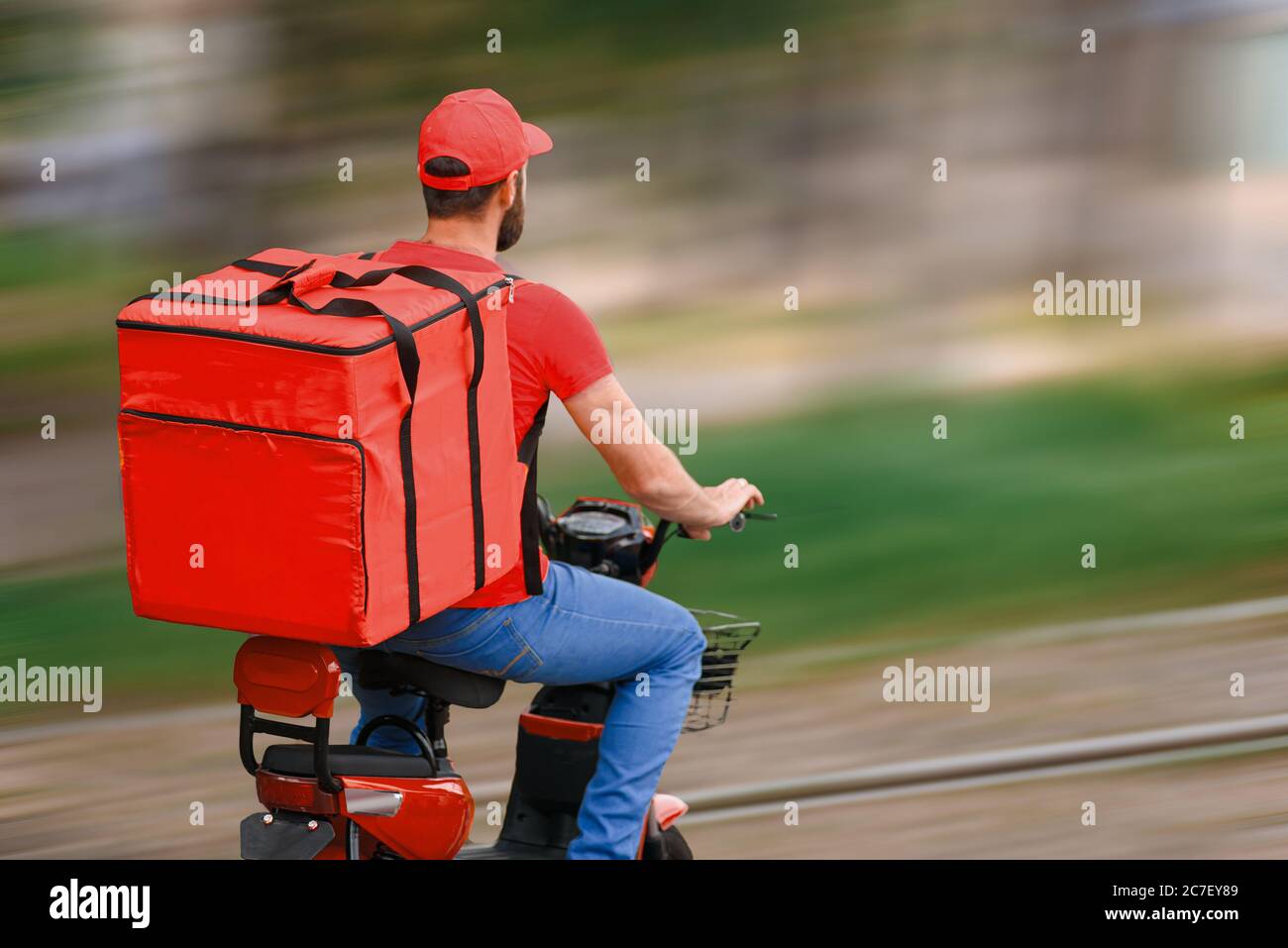 Un livreurs de nourriture en uniforme rouge roule dans un cyclomoteur avec un sac de livraison de nourriture. Vue de l'arrière. Banque D'Images
