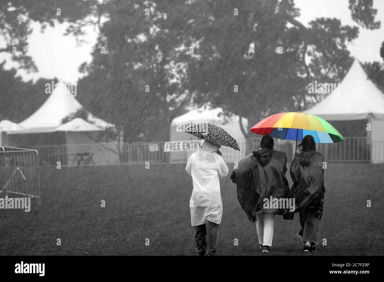 Plan horizontal de trois personnes avec imperméable un sombre et un parapluie de couleur arc-en-ciel Banque D'Images