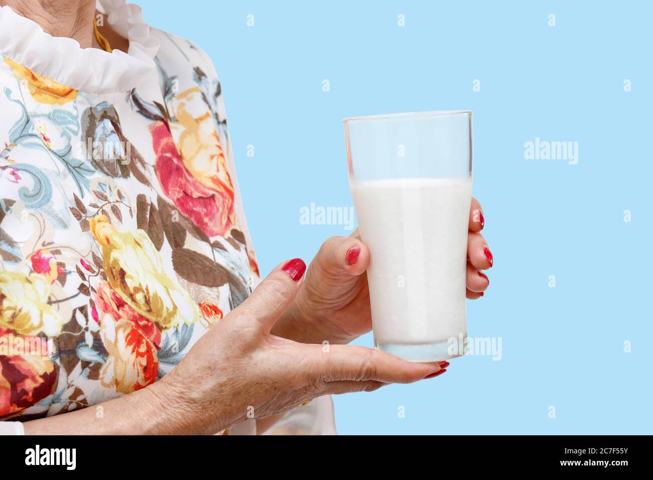 Femme âgée tenant un verre de lait sur fond bleu. Banque D'Images