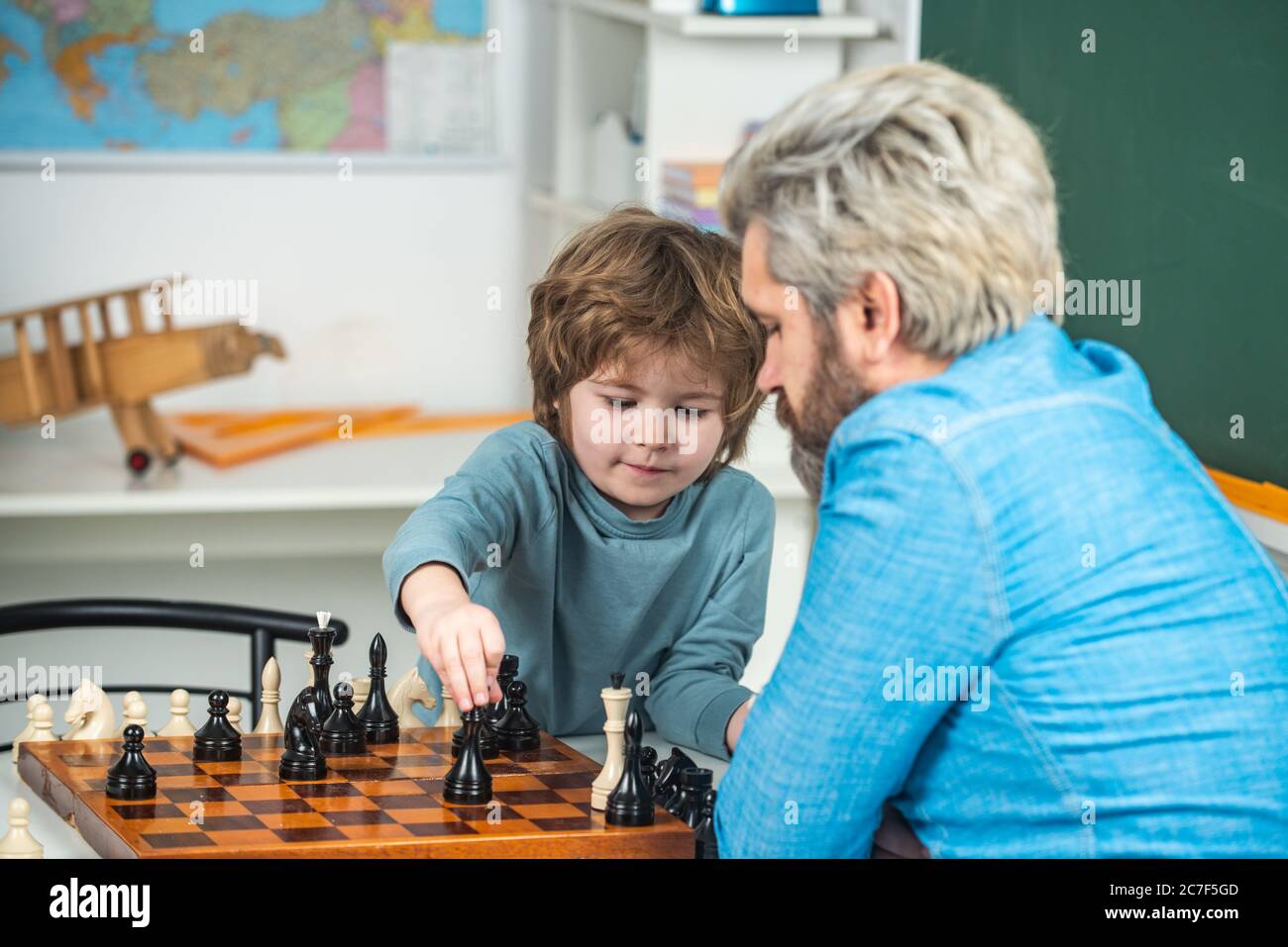 Générations hommes. Mignon petit garçon jouant aux échecs avec les parents. Joli petit garçon concentré assis à la table et jouant aux échecs avec son père Banque D'Images