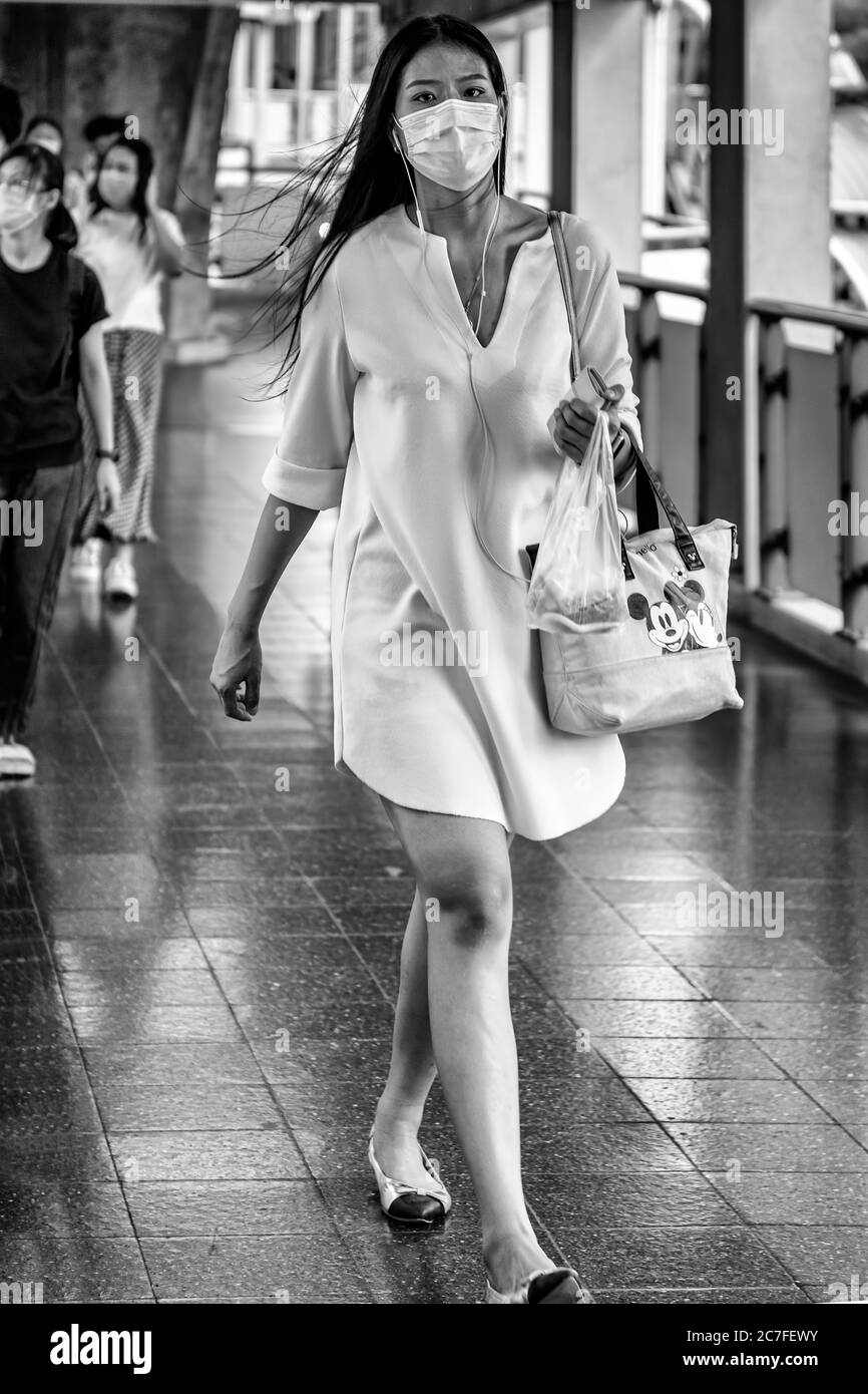 Femme portant un masque et des écouteurs marchant dans la rue pendant la pandémie de Covid 19, Bangkok, Thaïlande Banque D'Images