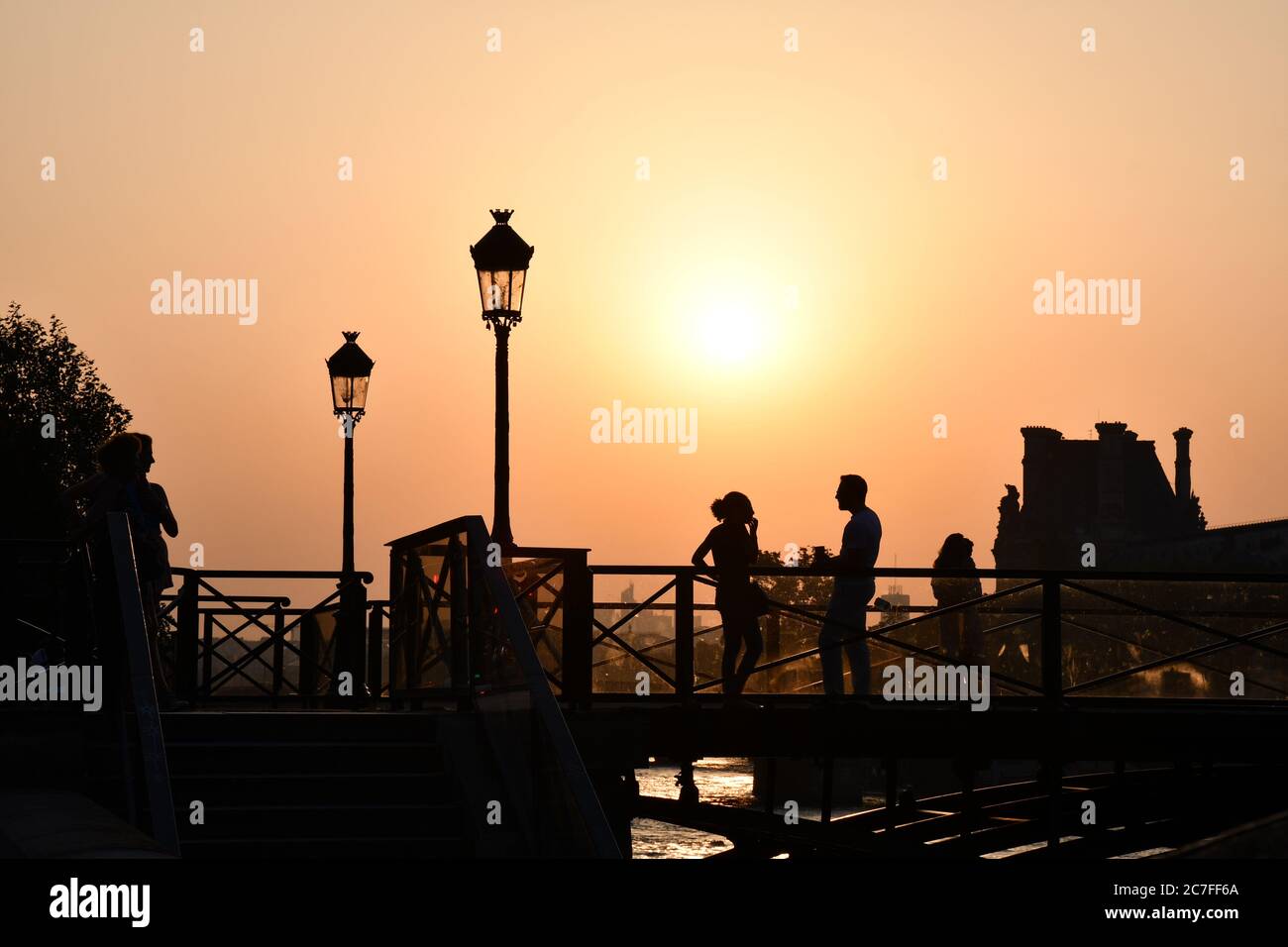 Silhouettes de personnes méconnaissables sur le pont au-dessus de la Seine devant la lumière du coucher du soleil. Lanterne vintage, lumières de rue sur fond de couleur orange Banque D'Images
