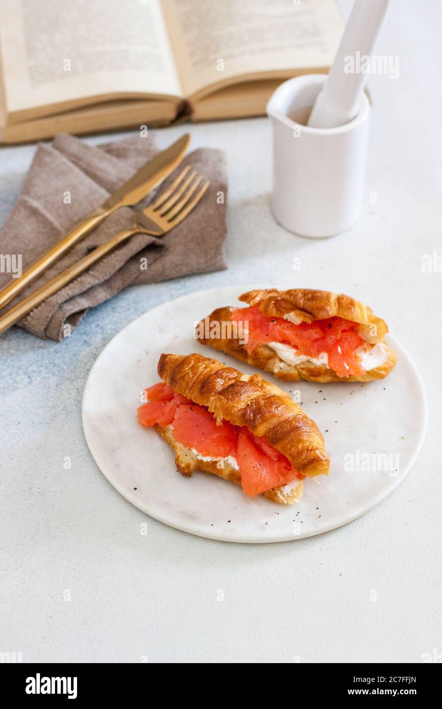 Délicieux petit déjeuner avec croissant, saumon fumé, fromage et poivre sur une assiette blanche. Ouverture de l'ancien livre en arrière-plan. Banque D'Images