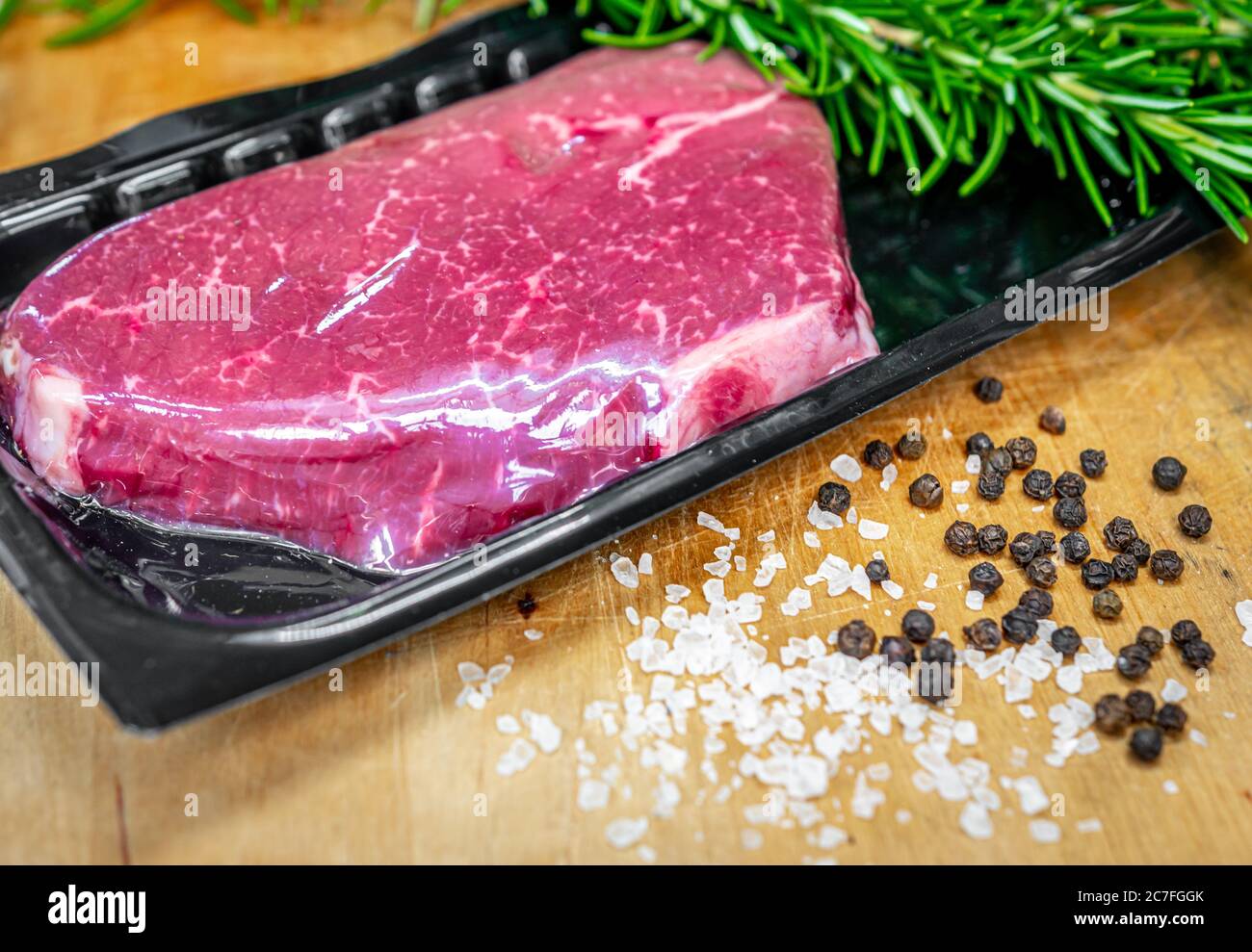 Steak de bœuf dans un emballage sous vide et épices sur planche à découper en bois Banque D'Images