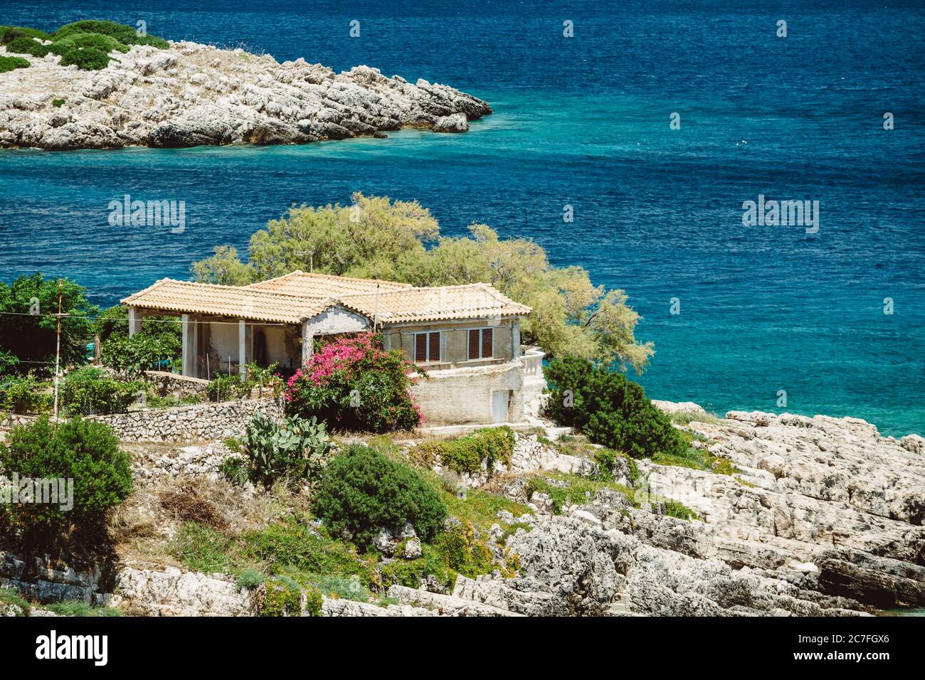 Maison en pierre sur le rivage de la mer Ionienne bleue sur la côte de l'île de Zakynthos avec des fleurs roses à l'avant pendant la journée ensoleillée d'été Banque D'Images