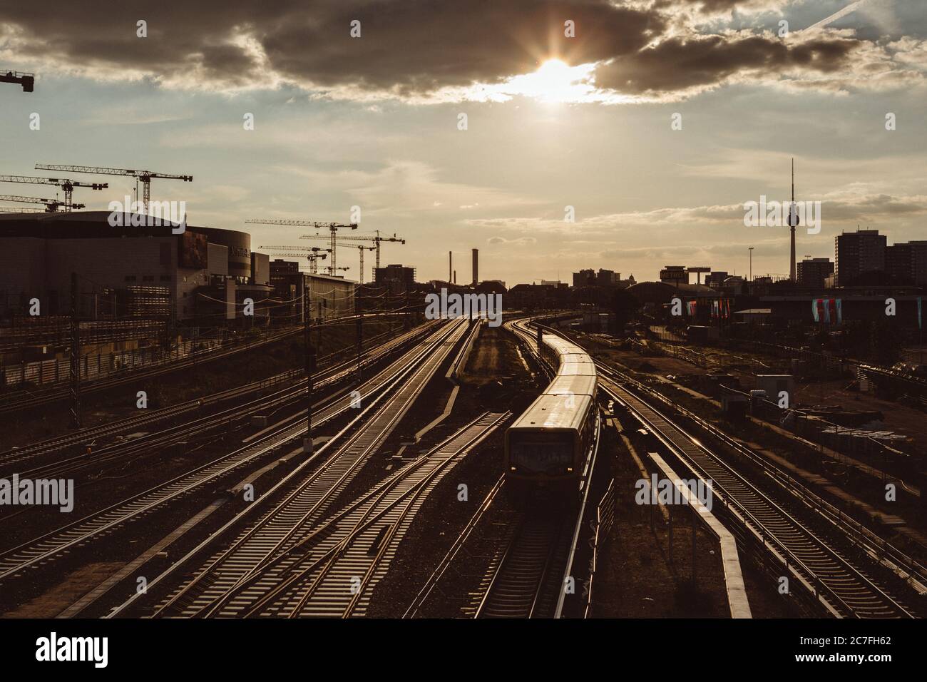 Train quittant la gare de Berlin avec le rétroéclairage du coucher de soleil doré, avec le chantier ferroviaire autour et la silhouette de la ville en arrière-plan Banque D'Images