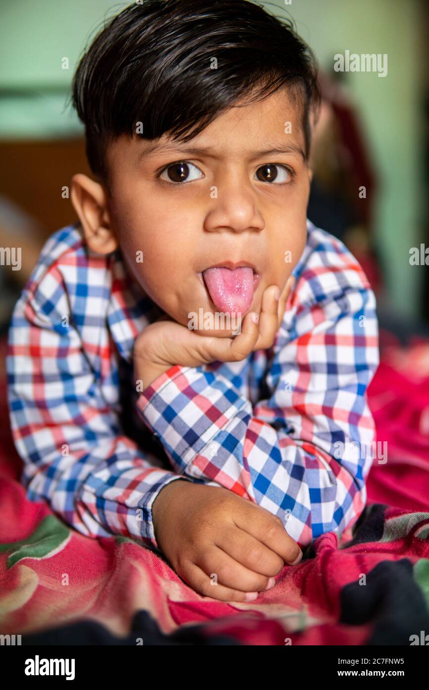 Portrait d'un petit garçon en colère mignon allongé sur le lit et collant sa langue tout en regardant l'appareil photo. Banque D'Images