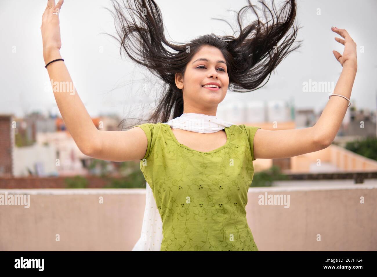 Belle, heureuse indienne jeune fille de tard en adolescence de jeter les cheveux dans l'air et de profiter de l'air frais en extérieur. Elle regarde et donne un sourire éclatant. Banque D'Images