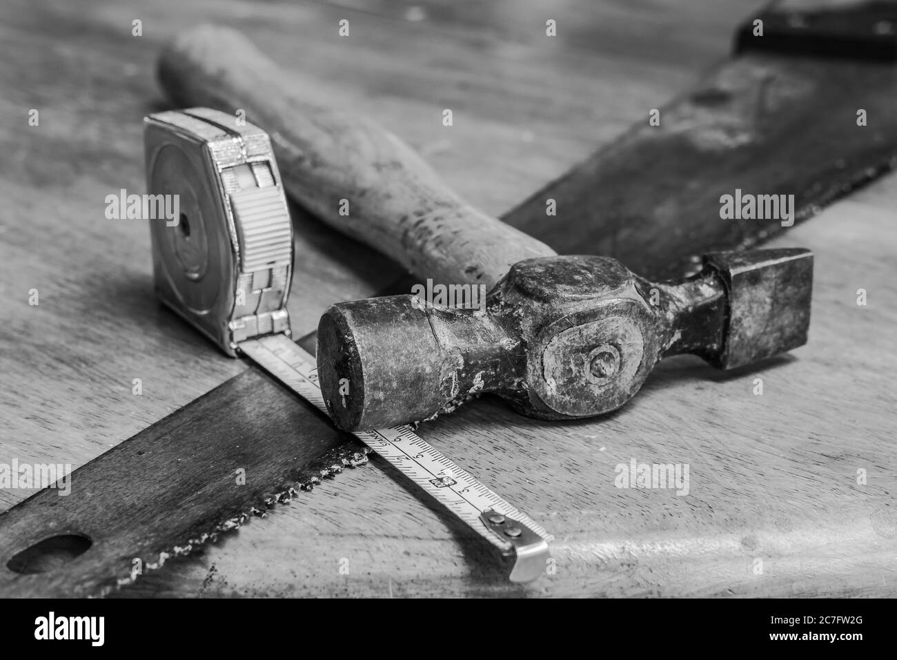 Gros plan, faible focale d'un mètre ruban étendu montrant les échelles. Il y a aussi un vieux marteau et une scie à bois vus sur une ancienne table d'atelier en bois. Banque D'Images