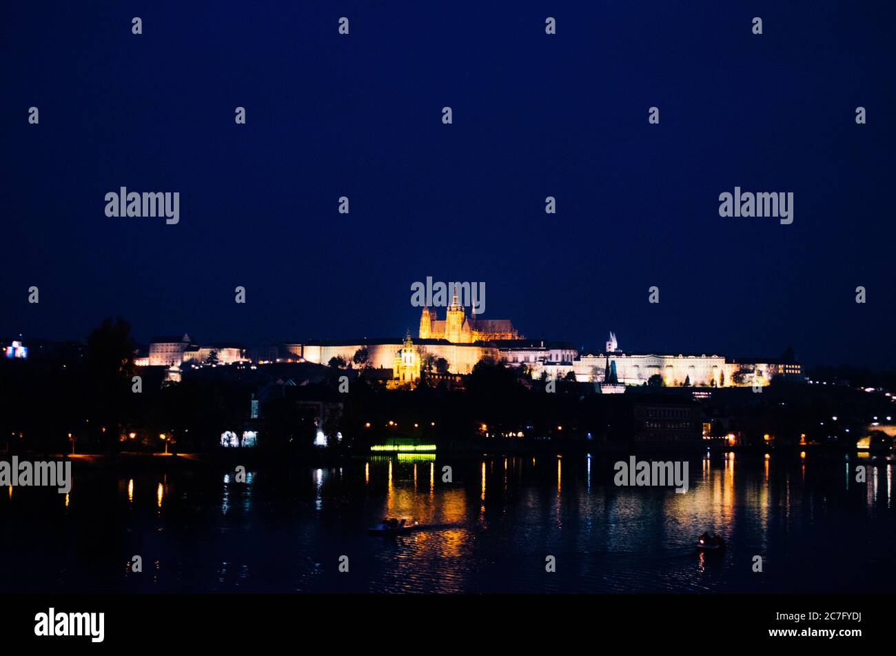 Une soirée sombre à Prague avec des lumières incandescentes illuminant la ville et des reflets sur la Vltava et le château de Prague à une distance. Banque D'Images