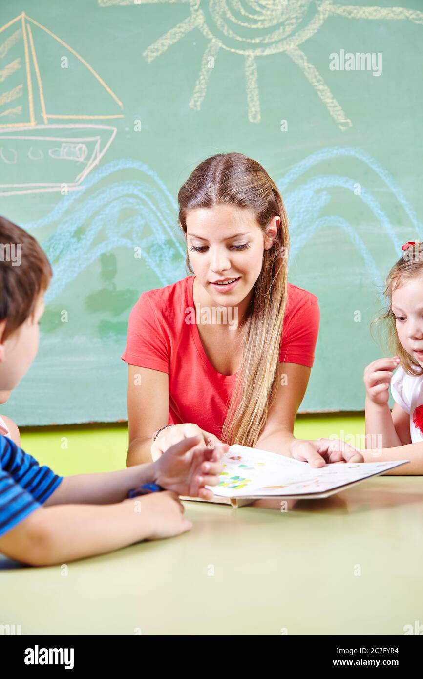 Un enseignant de maternelle et quelques enfants lisent un livre ensemble dans la maternelle Banque D'Images