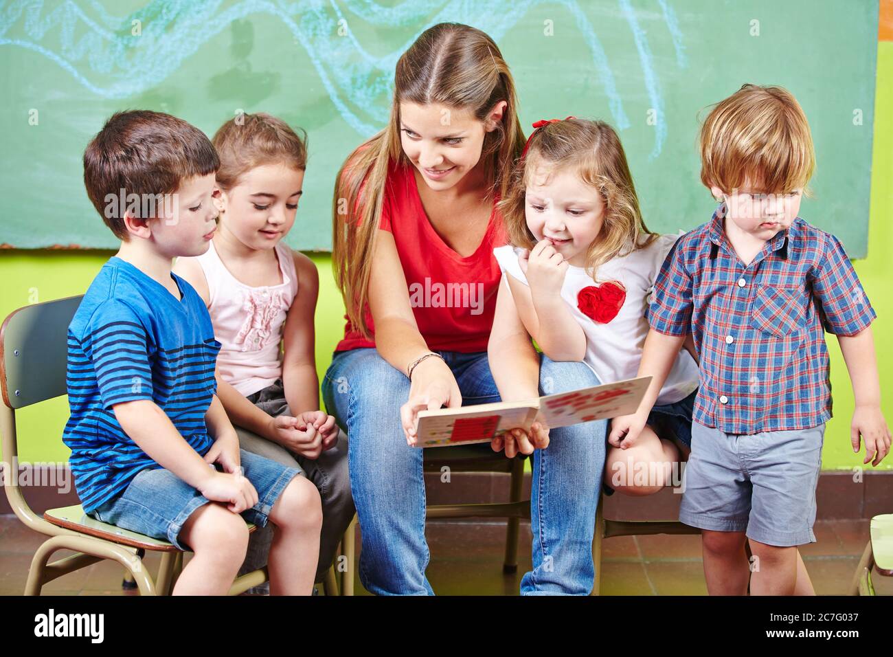 Des enfants heureux avec des éducateurs lisent un livre ensemble dans la maternelle Banque D'Images