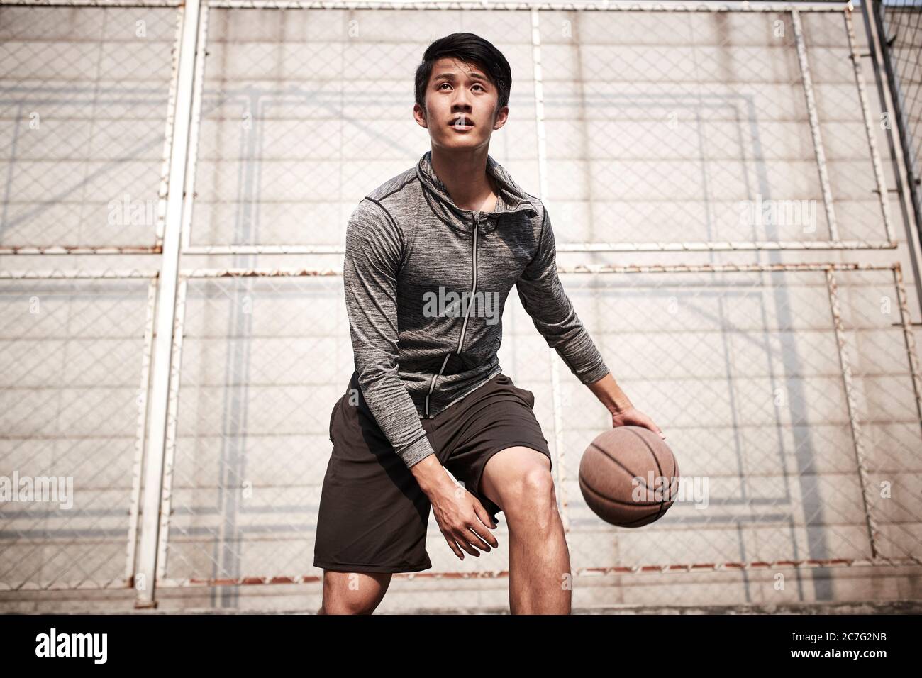 un jeune joueur de basket-ball asiatique s'entraîner à manipuler le ballon sur un terrain en plein air Banque D'Images