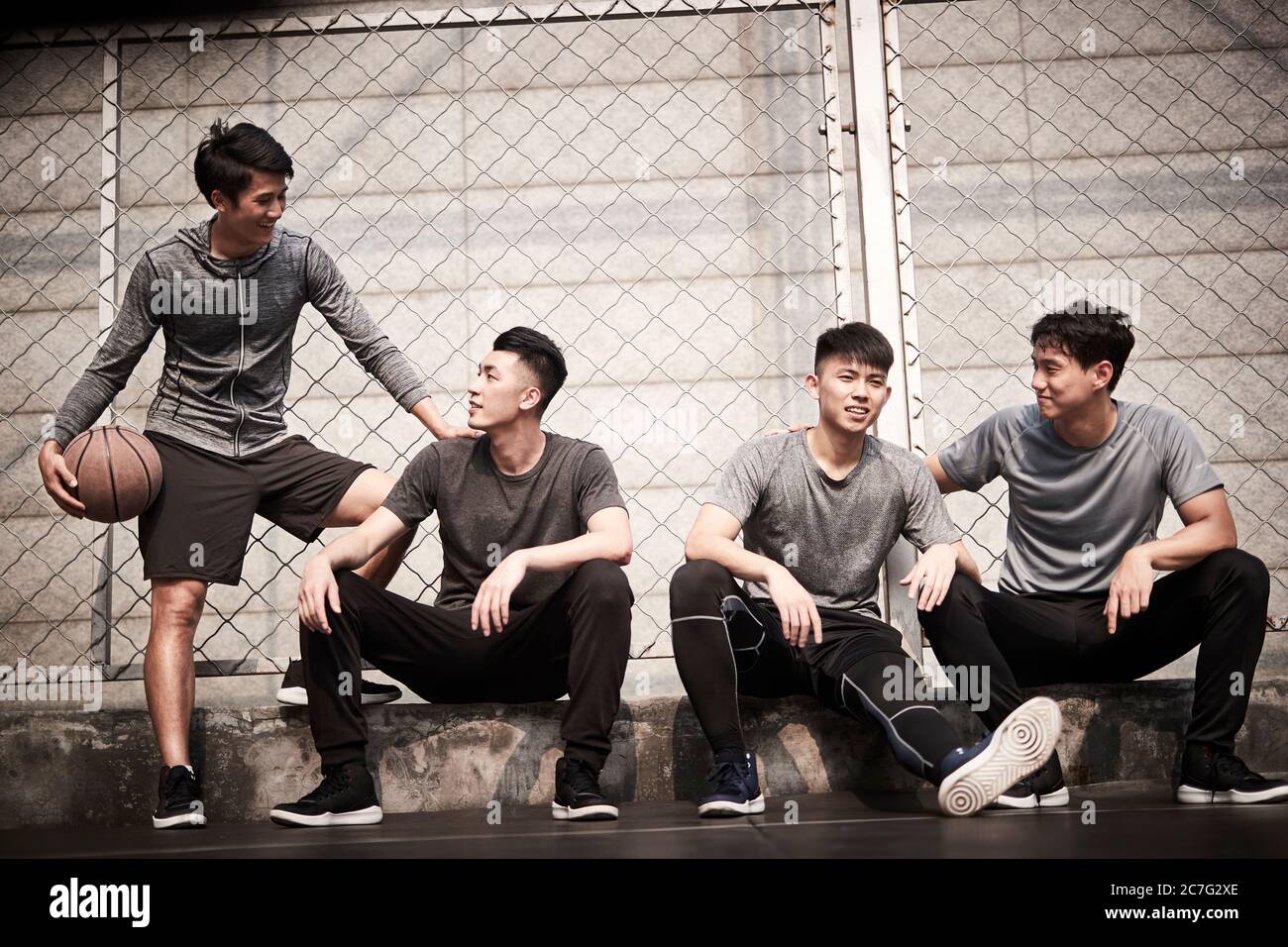 groupe de quatre jeunes hommes asiatiques se reposant sur un court de basket-ball extérieur pour discuter en toute tranquillité Banque D'Images