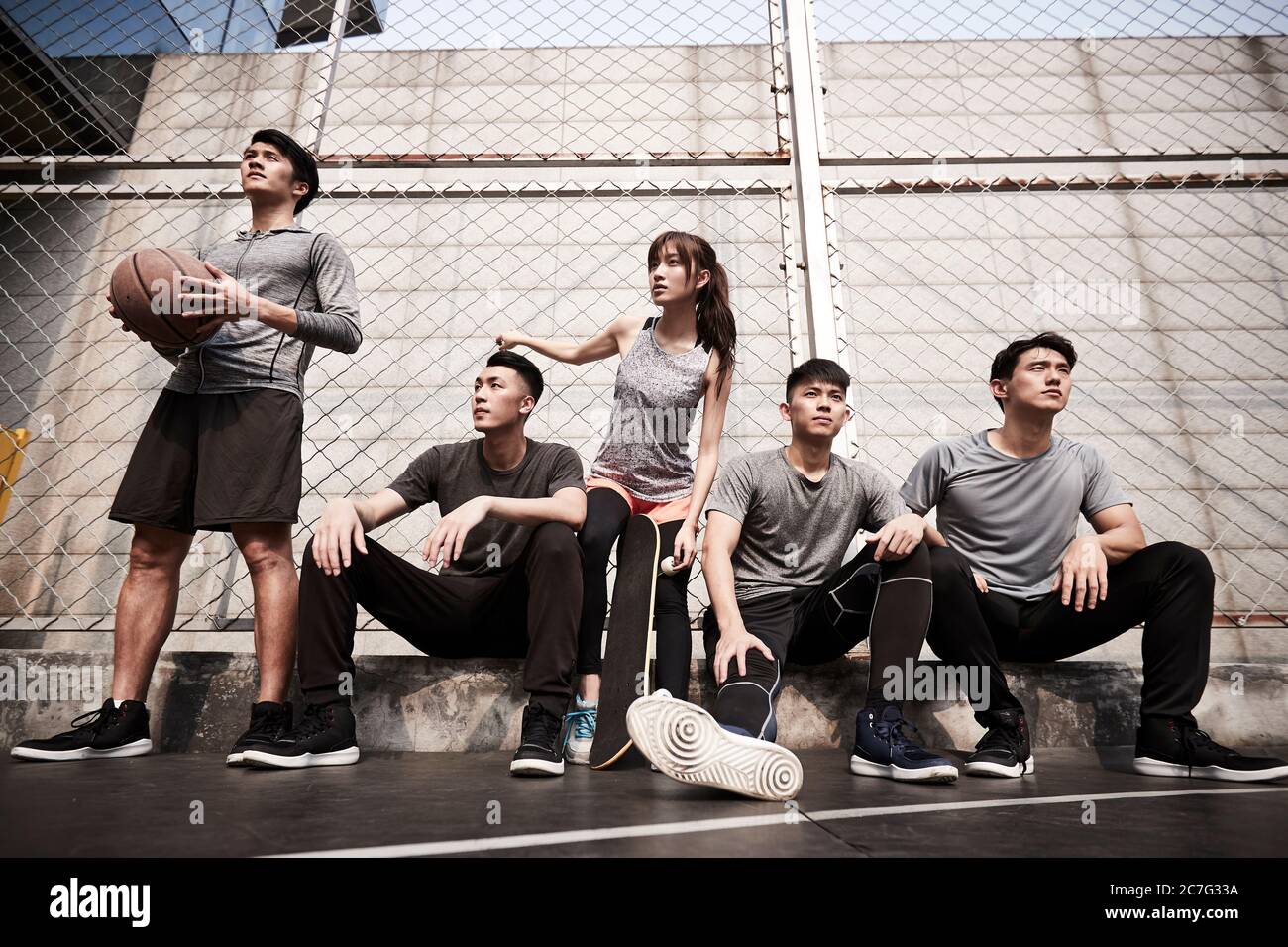 groupe de cinq jeunes adultes asiatiques, hommes et femmes, se reposant sur un terrain de basket-ball extérieur Banque D'Images
