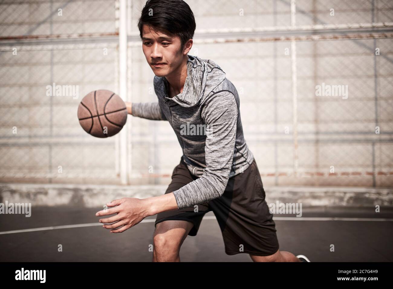 un jeune joueur de basket-ball asiatique s'entraîner à manipuler le ballon sur un terrain en plein air Banque D'Images