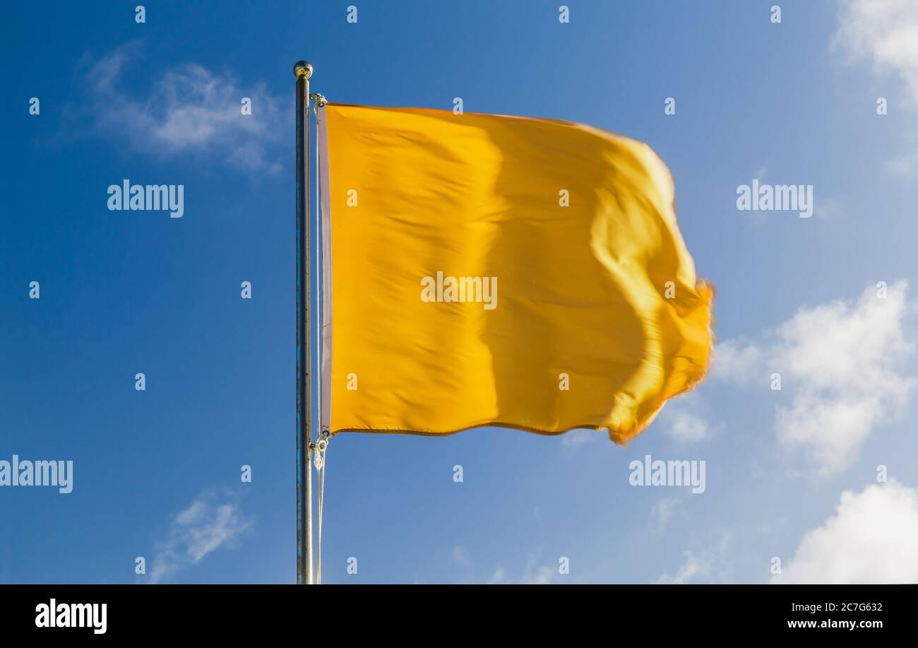 Drapeau jaune sur une station de sauveteurs de plage agitant sur un vent fort au-dessus du ciel bleu Banque D'Images