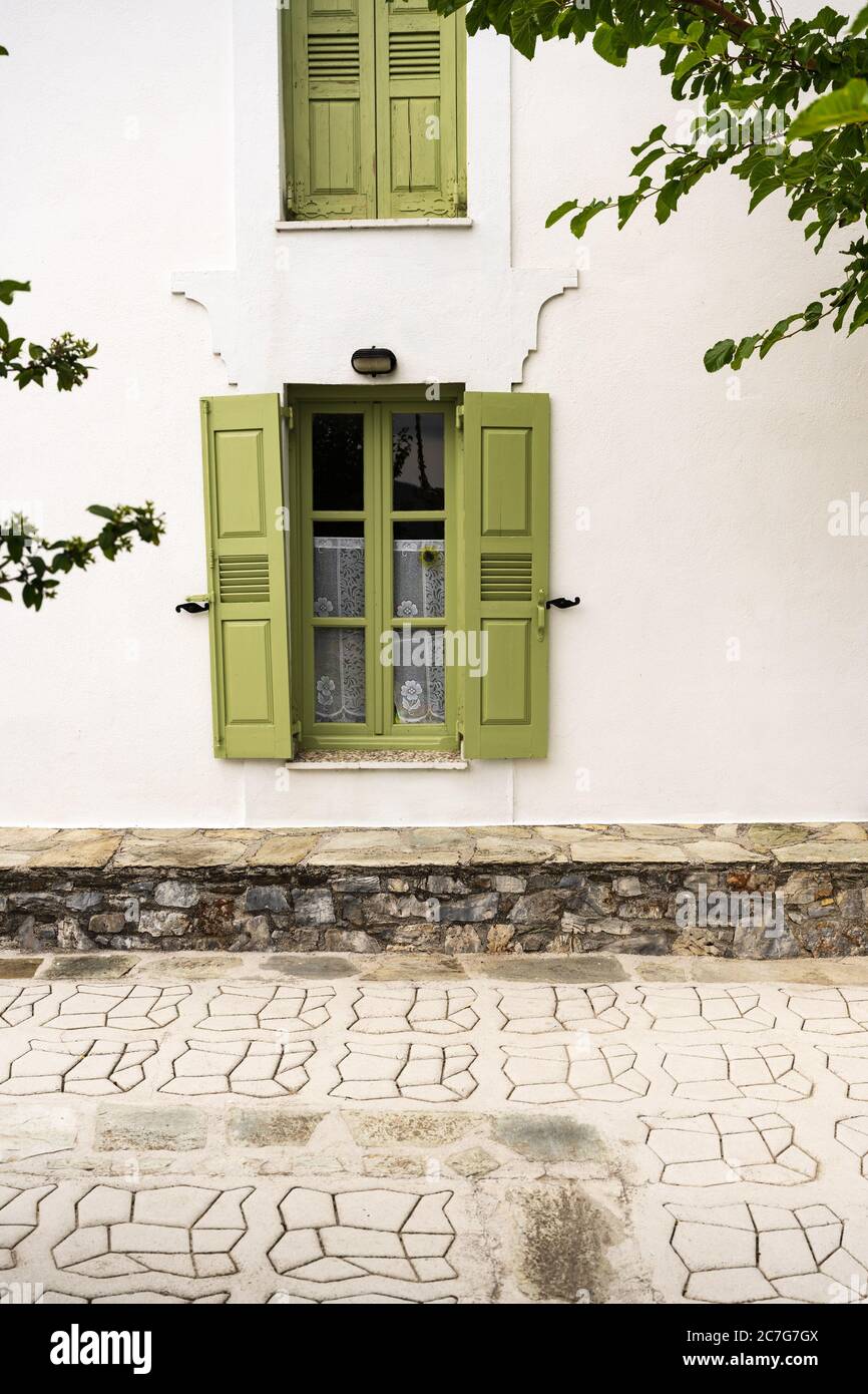 Un mur blanc avec des fenêtres aux volets verts d'une maison de campagne méditerranéenne et une terrasse lumineuse avec arbre. Banque D'Images