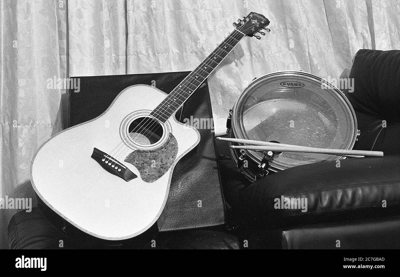Prise de vue en échelle de gris d'une guitare et d'un tambour avec des pilons de tambour sur un canapé en cuir Banque D'Images