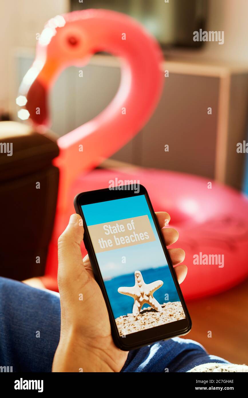jeune homme, portant des vêtements d'été décontractés, assis sur un fauteuil, ayant son smartphone entre ses mains avec le texte état des plages dans son écran, Banque D'Images