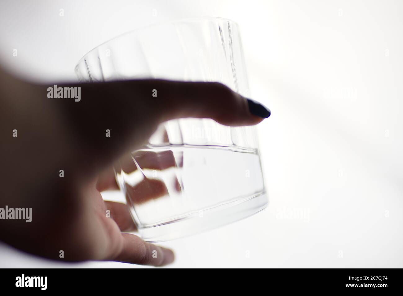 Un verre d'eau dans une main femelle sur un fond blanc isolé. Vue latérale, mise au point sélective. Banque D'Images