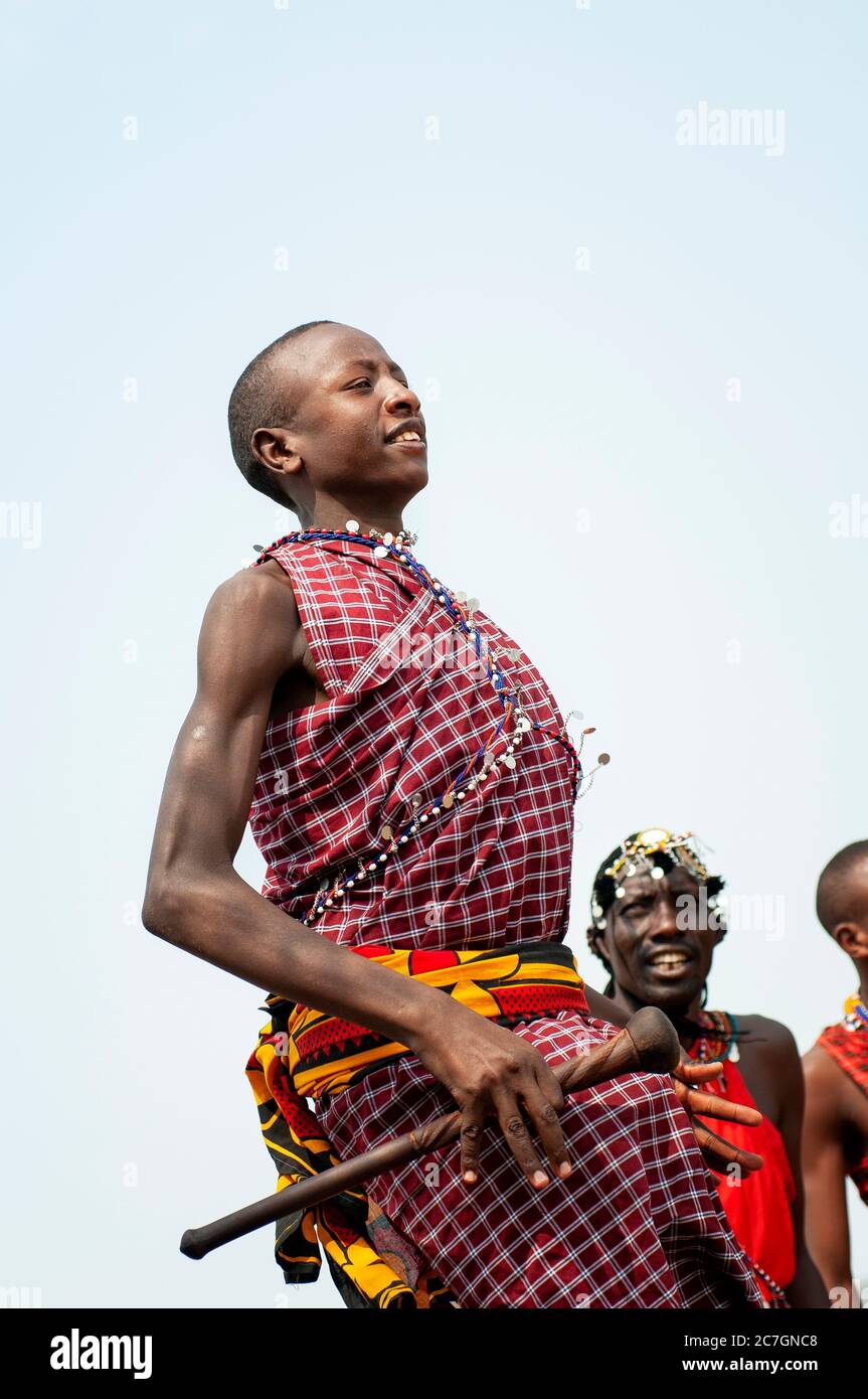 Homme de Maasai souriant portant une tenue traditionnelle, prenant part à la danse traditionnelle d'Adumu, ou danse de saut, dans la réserve nationale de Maasai Mara. Kenya. Banque D'Images