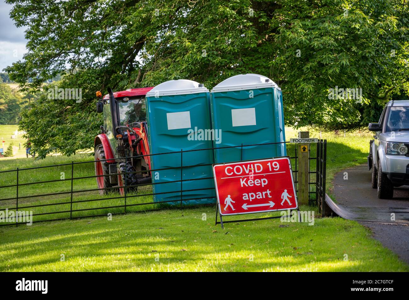 Deux toilettes portables en plastique derrière un panneau d'avertissement de distance Covid-19 lors d'un événement en plein air. Banque D'Images