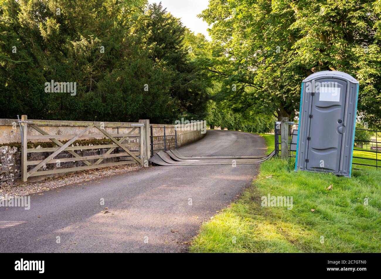 Une toilette portable en plastique à côté d'une grille de bétail couverte sur un sentier public dans un champ lors d'un événement en plein air. Banque D'Images