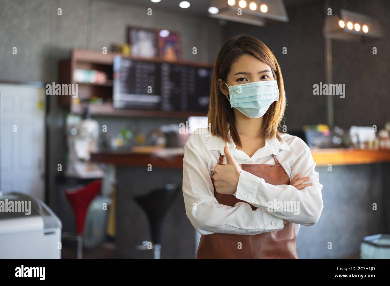 Nouveau démarrage normal petite entreprise Portrait de femme asiatique Barista portant un masque de protection se tenir dans son café tout en sociant distancé Banque D'Images