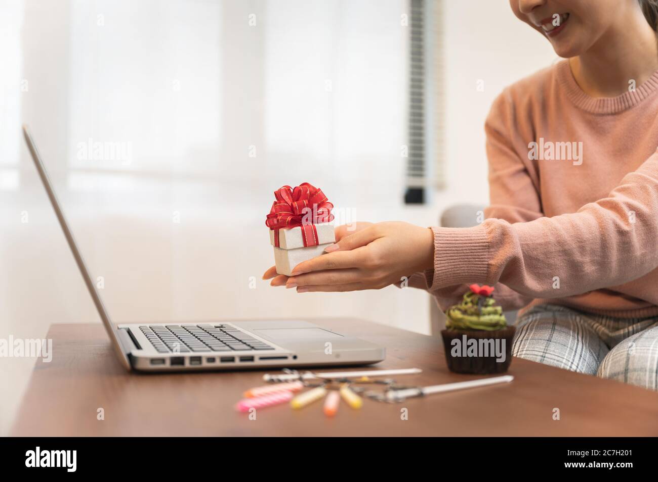 Femme asiatique célébrant l'anniversaire de ses collègues par appel vidéo en ligne, tenant sa boîte cadeau à portée de main tout en restant isolée chez elle Banque D'Images
