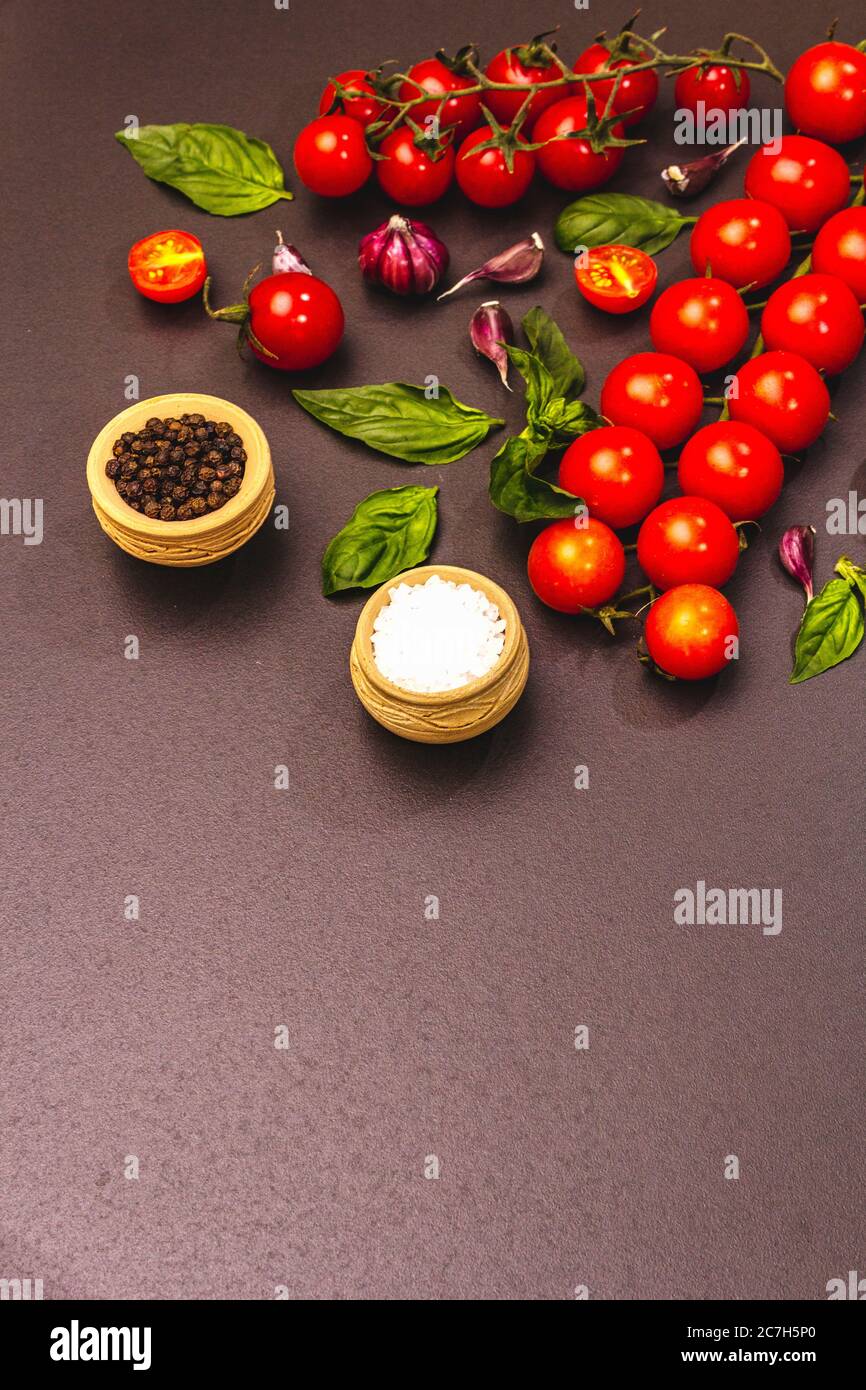 Concept de cuisine. Tomates cerises mûres, ail, basilic, sel et grains de poivre noir. Arrière-plan en béton noir et en pierre, espace de copie Banque D'Images