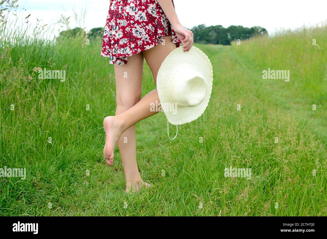 Une fille pieds nus marchant sur l'herbe verte. Femme avec jupe colorée, tenant le chapeau d'été à la main. Été en Pologne, belle terre agricole en Basse Silésie. Banque D'Images